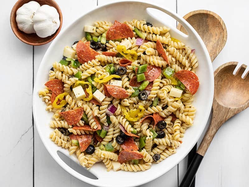 Overhead view of pizza pasta salad in a serving bowl with wooden salad utensils on the side