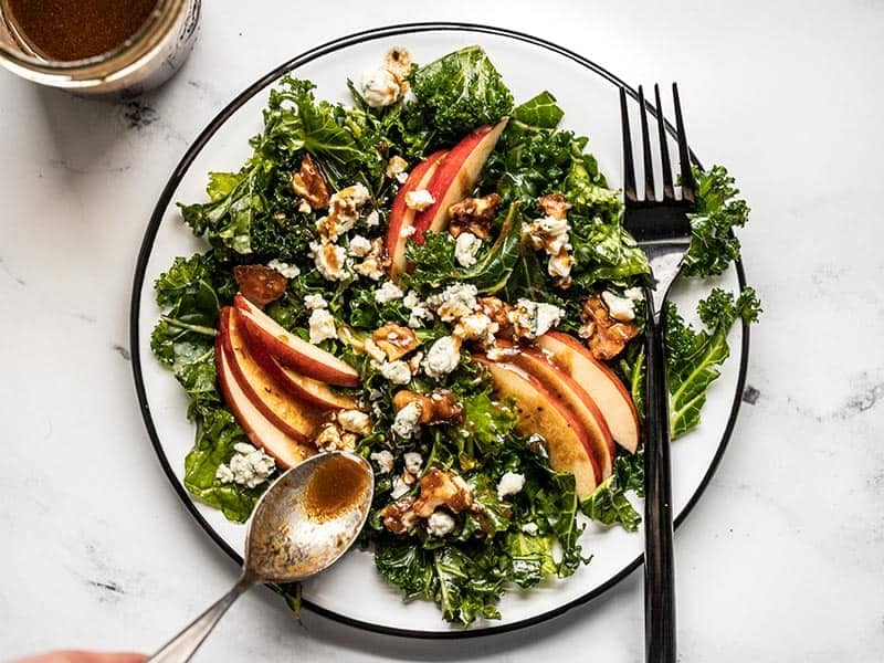 Balsamic vinaigrette being drizzled over an Autumn Kale and Apple Salad with a spoon