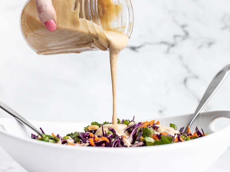 Sesame ginger dressing being poured over crunchy cabbage salad from a mason jar