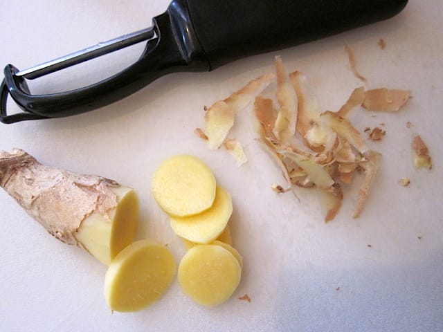 fresh ginger with peeler and sliced on counter 
