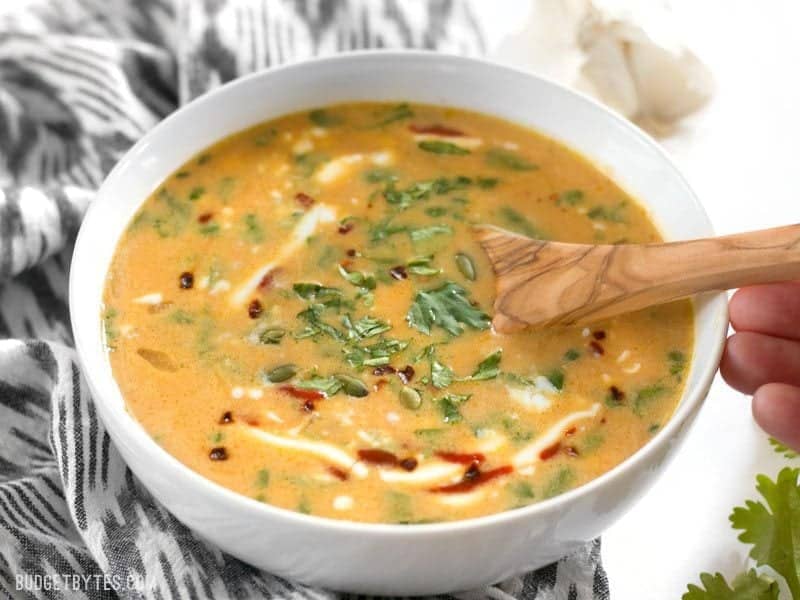 White bowl full of Spicy Coconut and Pumpkin Soup with spoon 