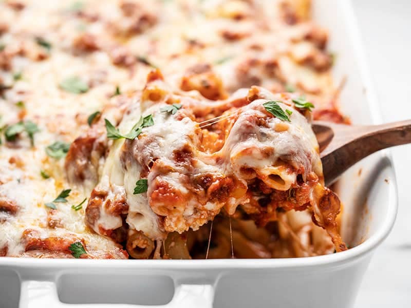 Front view of a wooden spoon lifting a scoopful of Baked Ziti from the casserole dish