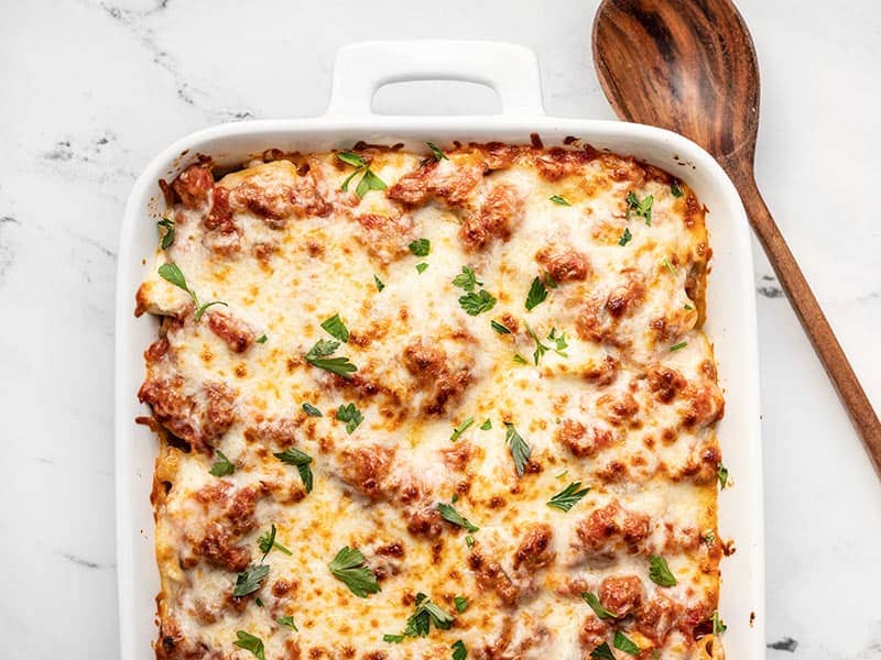 Finished baked ziti casserole topped with chopped parsley and a wooden spoon on the side