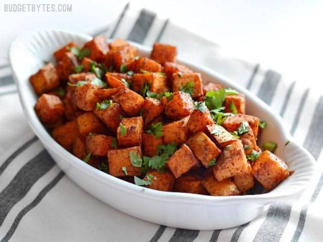 Side view of a white serving dish full of Chili Roasted Sweet Potatoes garnished with cilantro