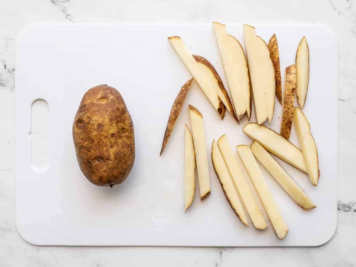 Two russet potatoes on a cutting board, one cut into fries