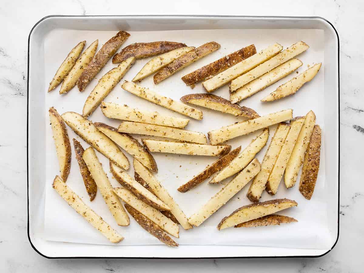 uncooked fries spread out on a parchment lined baking sheet