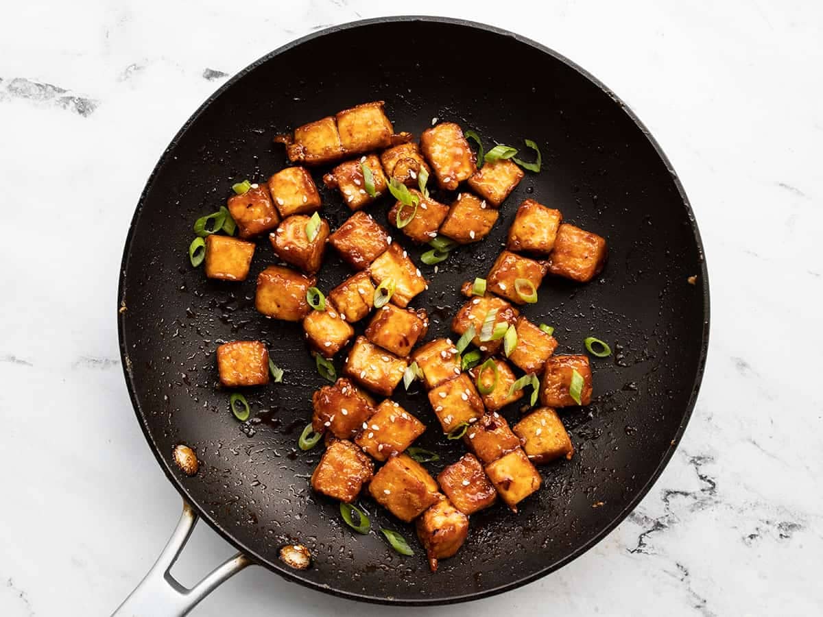 finished honey sriracha tofu in the skillet garnished with sliced green onions