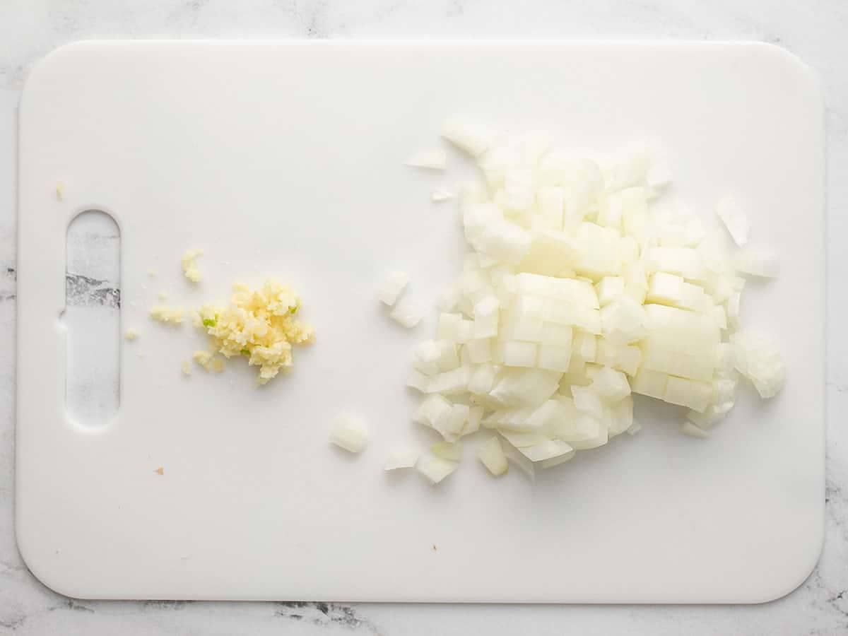 Chopped onion and garlic on a cutting board.