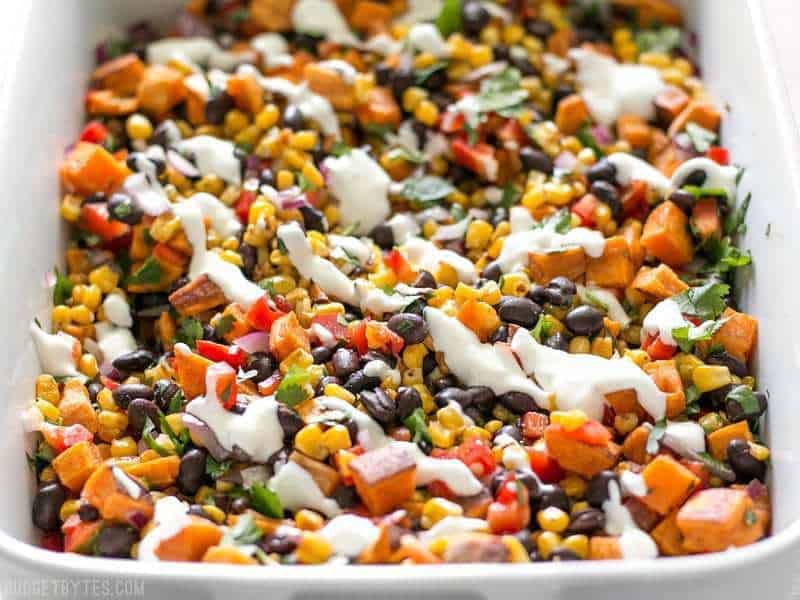 Roasted Sweet Potato Rainbow Salad in a large serving dish, from the front, with lime crema drizzled on top