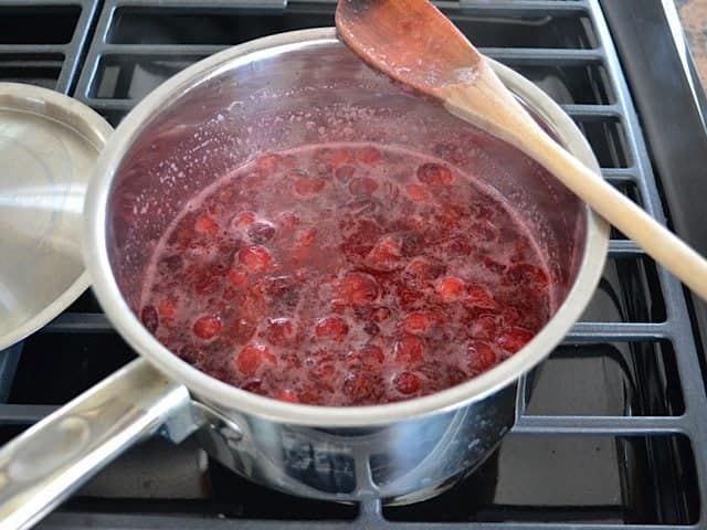 Boiled Cranberries in pot with softened gelatin stirred in, wooden spoon sitting on top of pot 