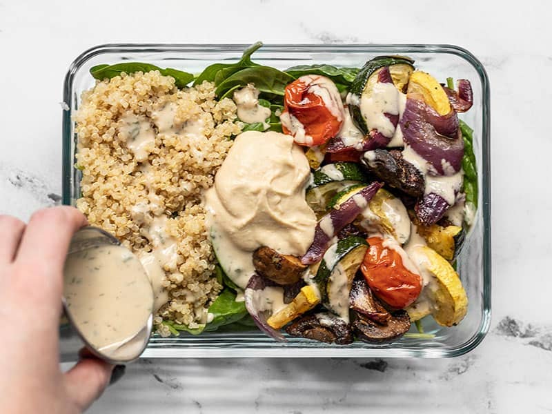 Dressing being poured onto a Roasted Vegetable Salad Meal Prep container