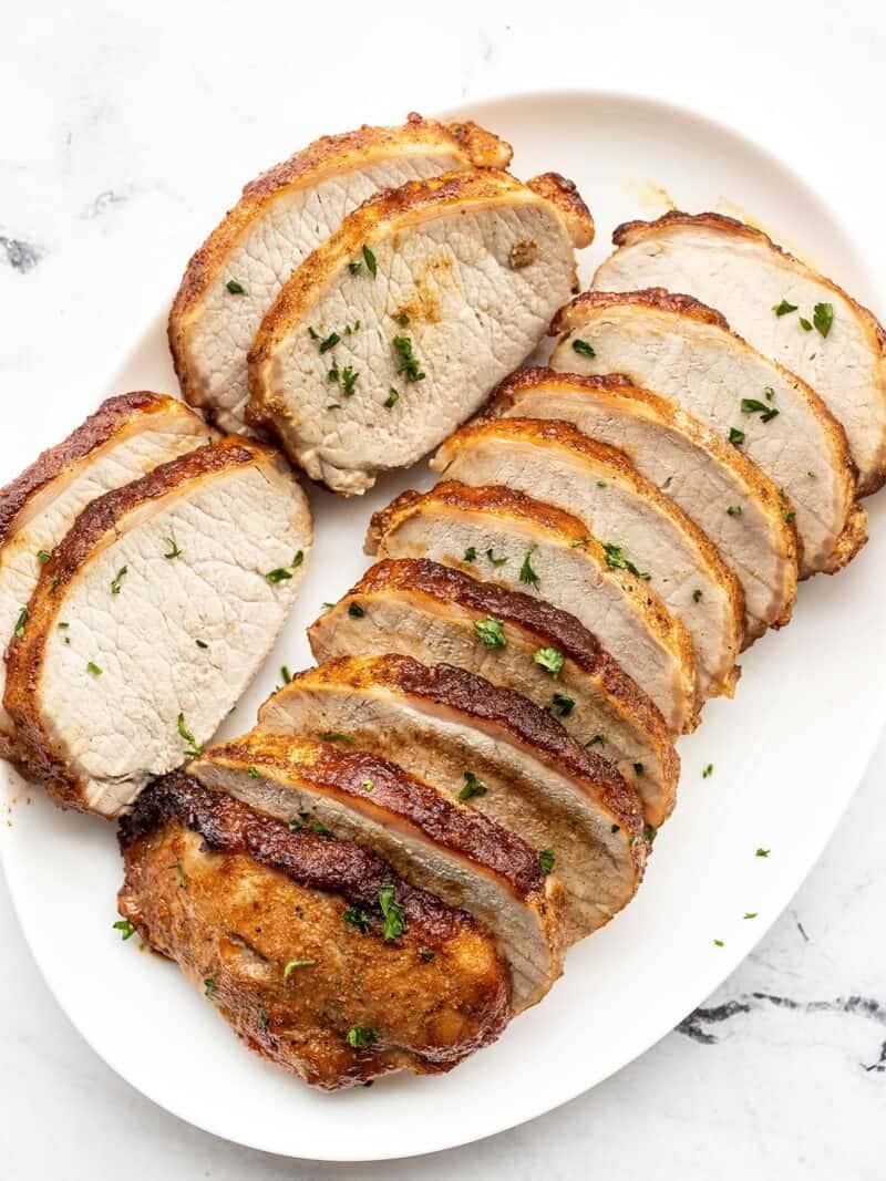 Slices of brown sugar roasted pork loin on a white oval serving dish