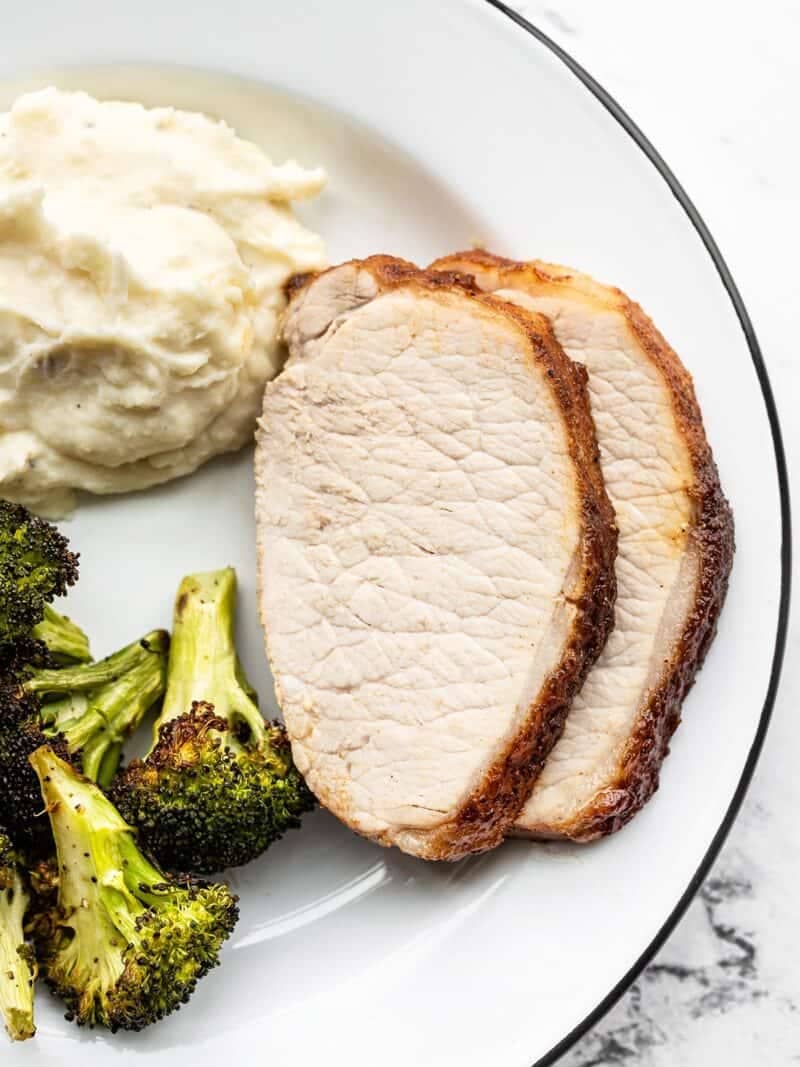 Two slices of roasted pork loin on a plate with broccoli and mashed potatoes