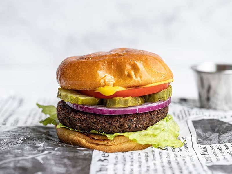 Side view of a single black bean burger on a bun, fully dressed, sitting on newsprint