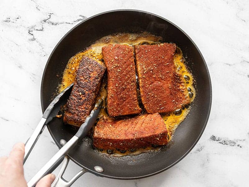 Blackened salmon being turned with tongs in the skillet