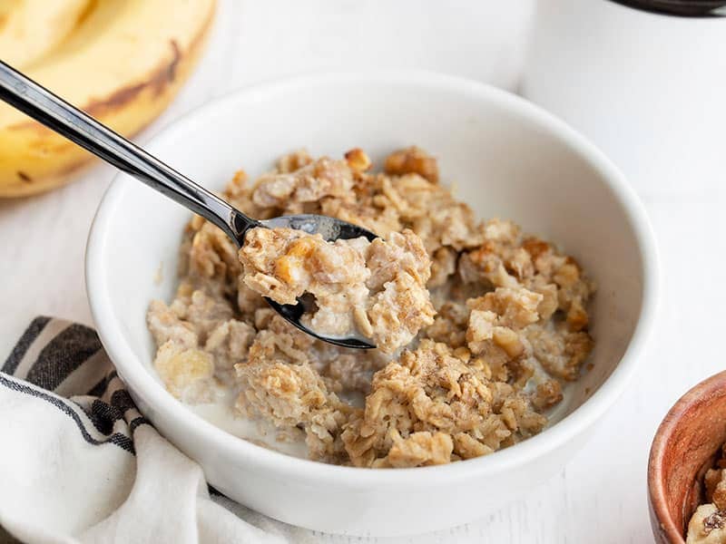 Side view of a bowl of banana bread baked oatmeal with a spoon lifting a bite