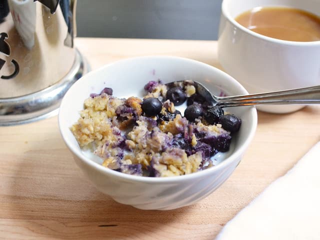 Bowl of Blueberry Banana Baked Oatmeal with a cup of coffee in the background 