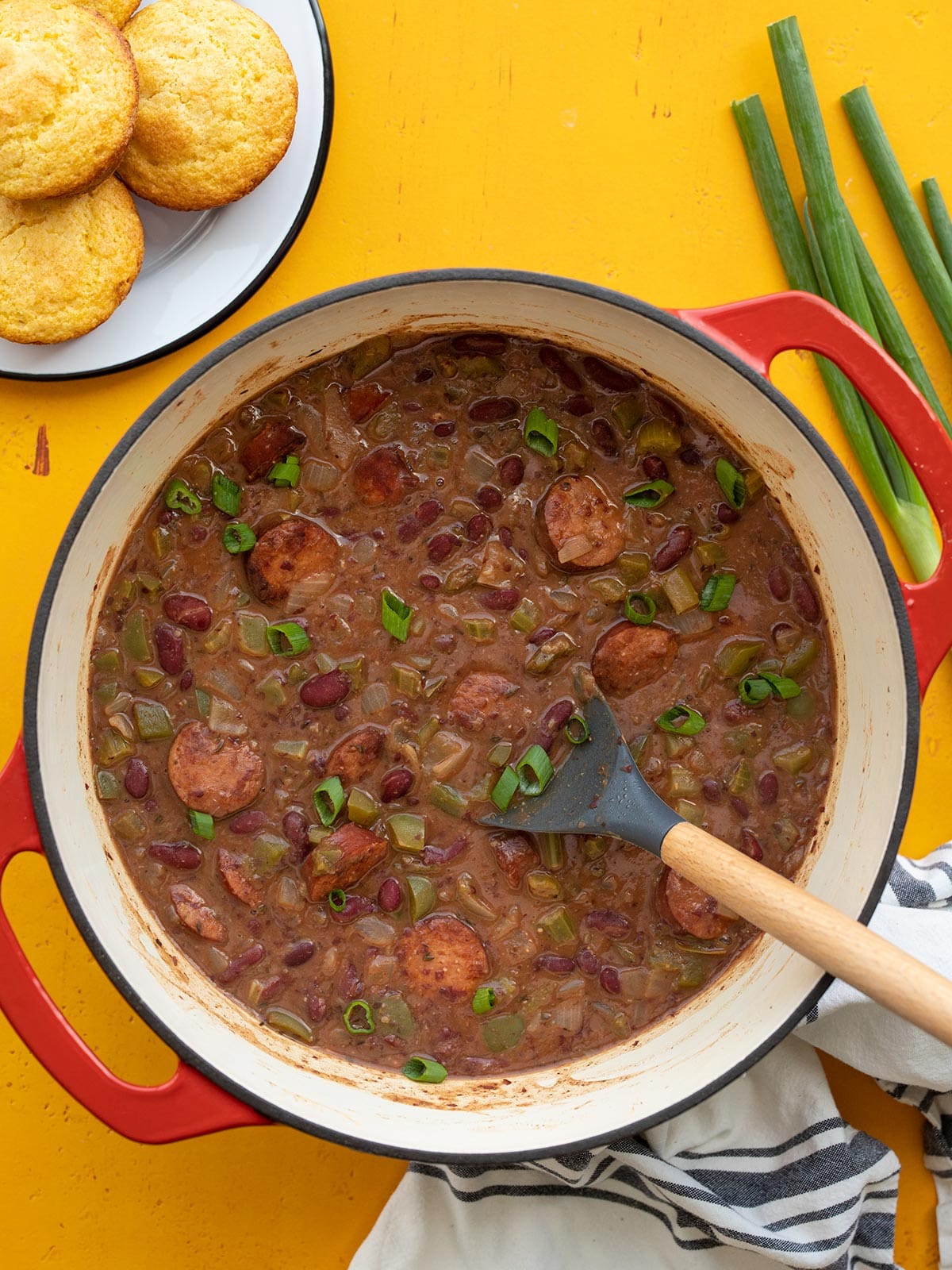 Overhead view of a pot of red beans with sausage, corn muffins on the side