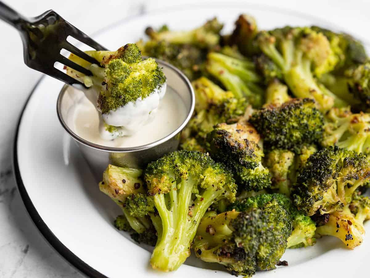 A roasted broccoli floret being dipped into a dish of ranch dressing