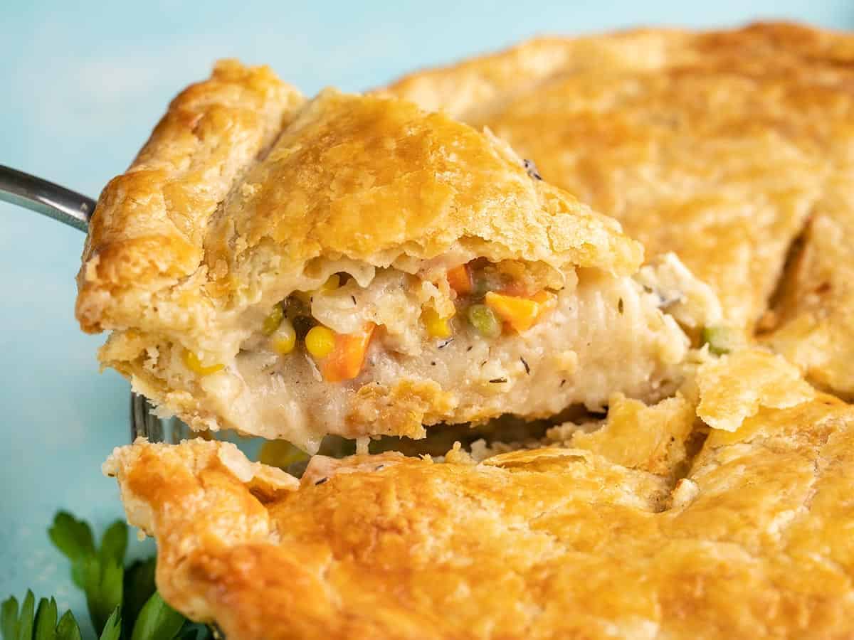 A slice of chicken pot pie being lifted out of the pie pan from the side.