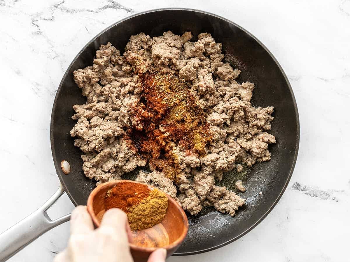 ground turkey cooking in a skillet with taco seasoning being sprinkled over top
