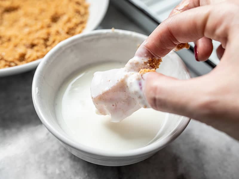 A piece of chicken being dipped into the yogurt slurry.