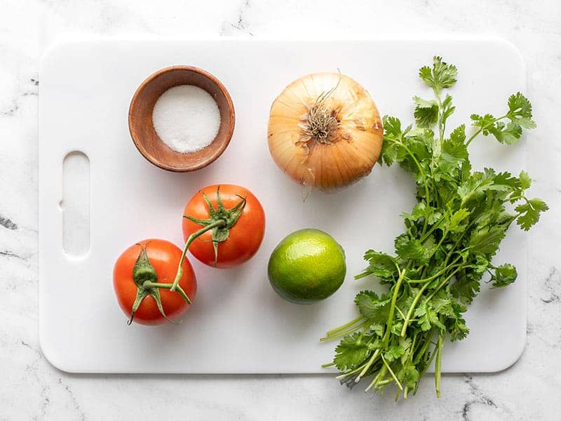 Fresh tomato, onion, lime, cilantro and salt on a cutting board