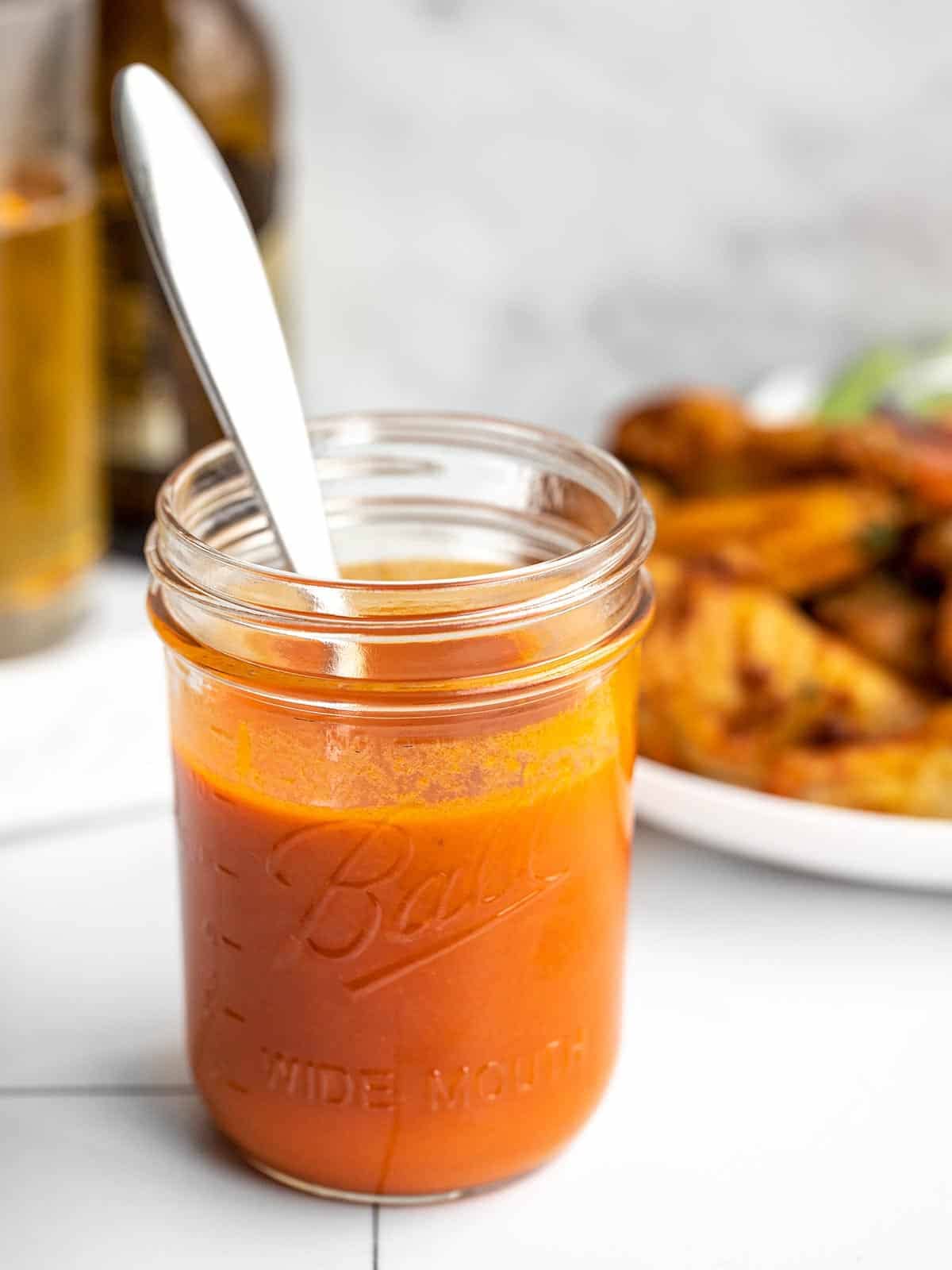 Buffalo sauce in a jar with wings in the background