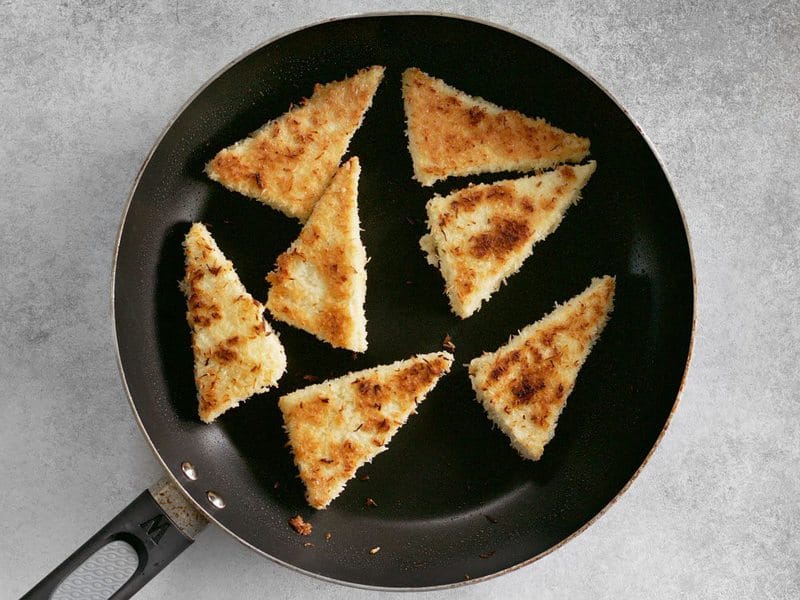 Fry coconut crusted tofu triangles in a skillet