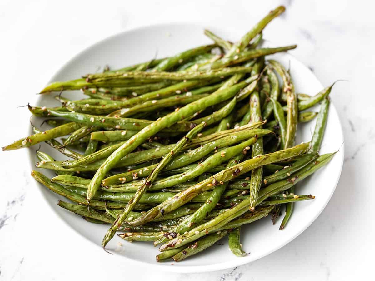 Side view of sesame roasted green beans in a shallow bowl.