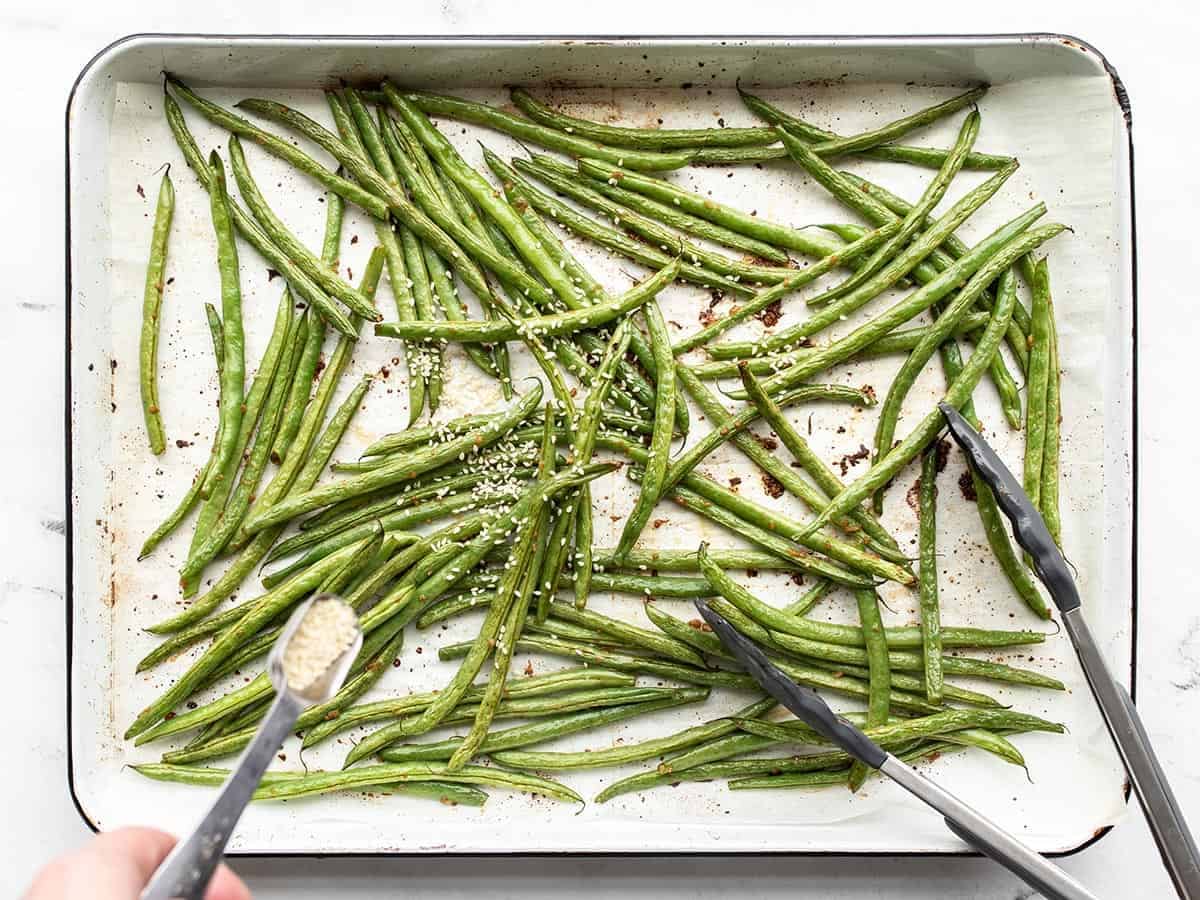 Mostly roasted green beans, sesame seeds being sprinkled on top