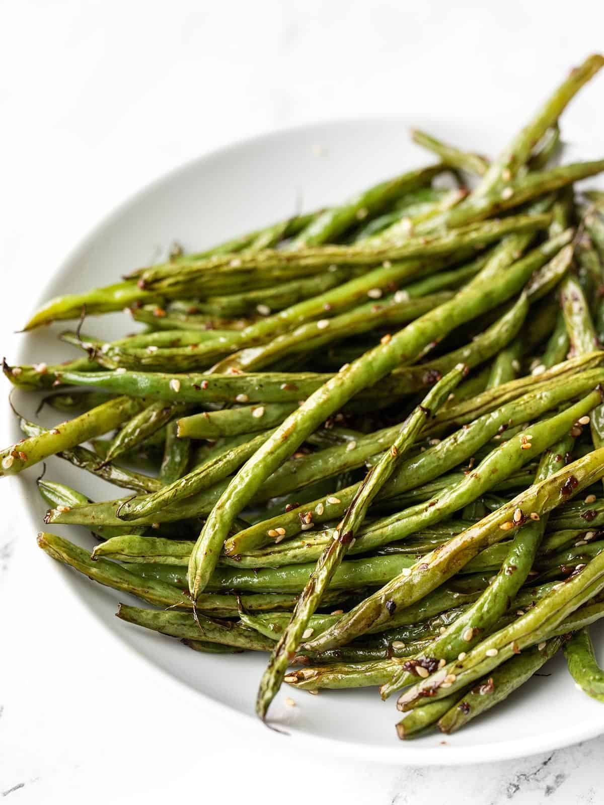 Close up side view of sesame roasted green beans in a shallow bowl