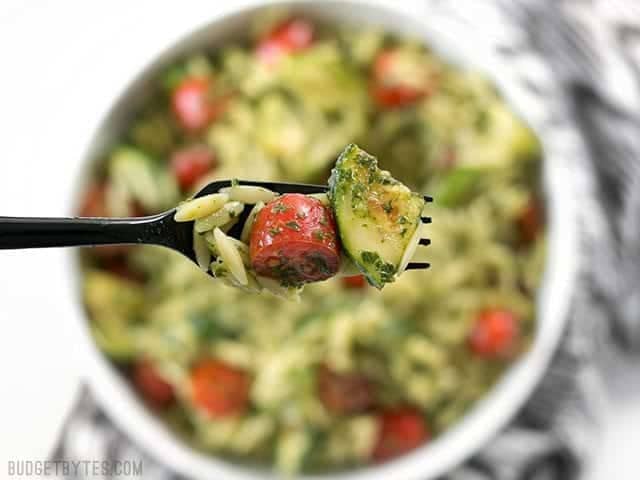 Close up of a forkful of Zucchini and Orzo Salad with Chimichurri with the bowl in the background