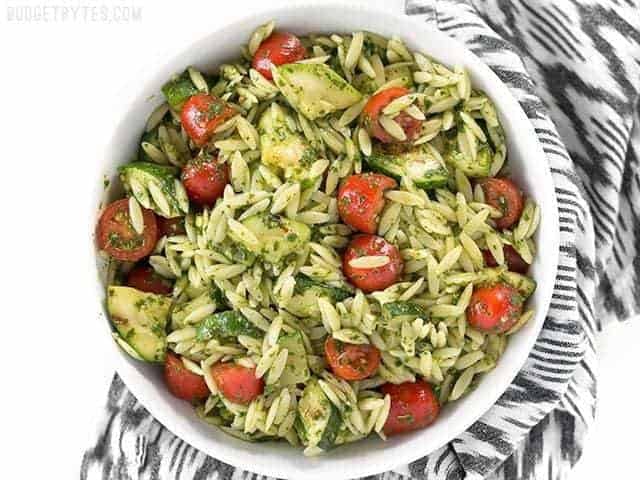 Overhead view of a bowl of Zucchini and Orzo Salad with Chimichurri sitting on a black and white striped napkin.