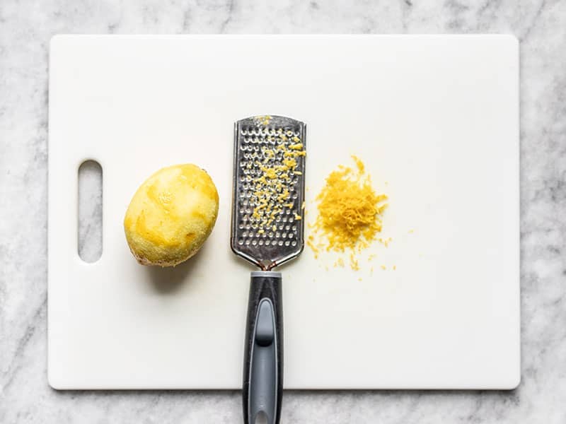 A zested lemon on a cutting board with a zester