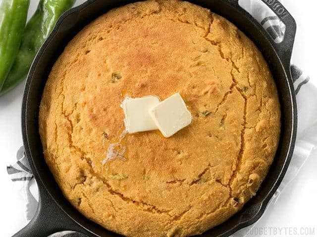 Top view of Hatch Chile Sweet Potato Cornbread in cast iron skillet, two cubes of butter on top 