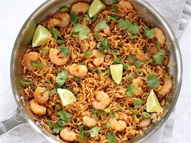 Finished Lime Shrimp Dragon Noodles in the skillet garnished with lime wedges and fresh cilantro